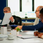 African businesswoman reading documents, signing its while business partners sharing paperwork sitting at conference table in broadroom. Executive director meeting shareholders in start up office