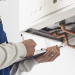 Professional plumber checking a boiler at home and writing on a clipboard